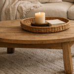 Round wooden coffee table on a beige carpet with a wicker tray holding a lit candle and a small book; cozy living room setting