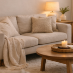 Cozy living room with a beige sofa, knitted throws, and a lit candle on a round wooden coffee table.
