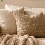 Cozy beige living room scene with a chunky knitted cream throw draped over a sofa and textured pillows nearby.